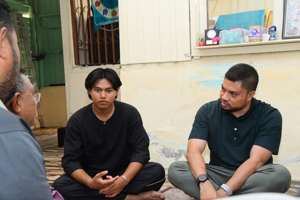 Dua orang pemuda duduk bersila dan mendengar perbualan bersama tetamu semasa Program Ziarah Kasih.
