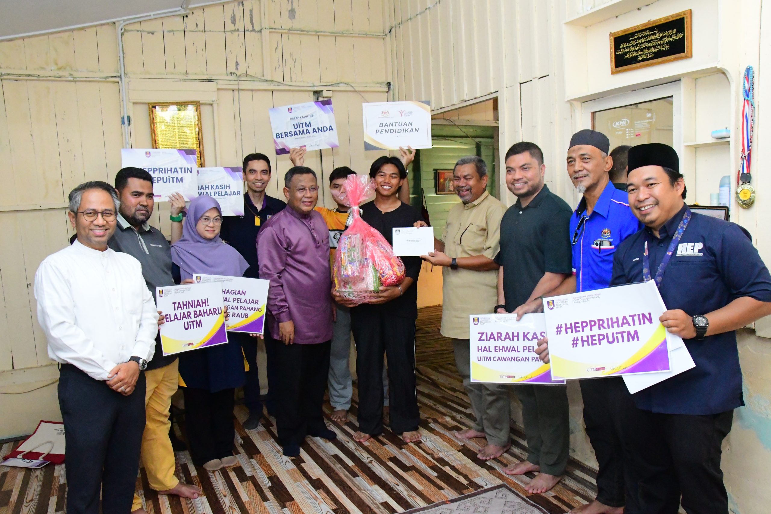 Muhammad Edriez bersama para tetamu dan wakil yang hadir ke Program Ziarah Kasih bergambar sambil memegang plakad, dengan bakul barangan bantuan di hadapan mereka.