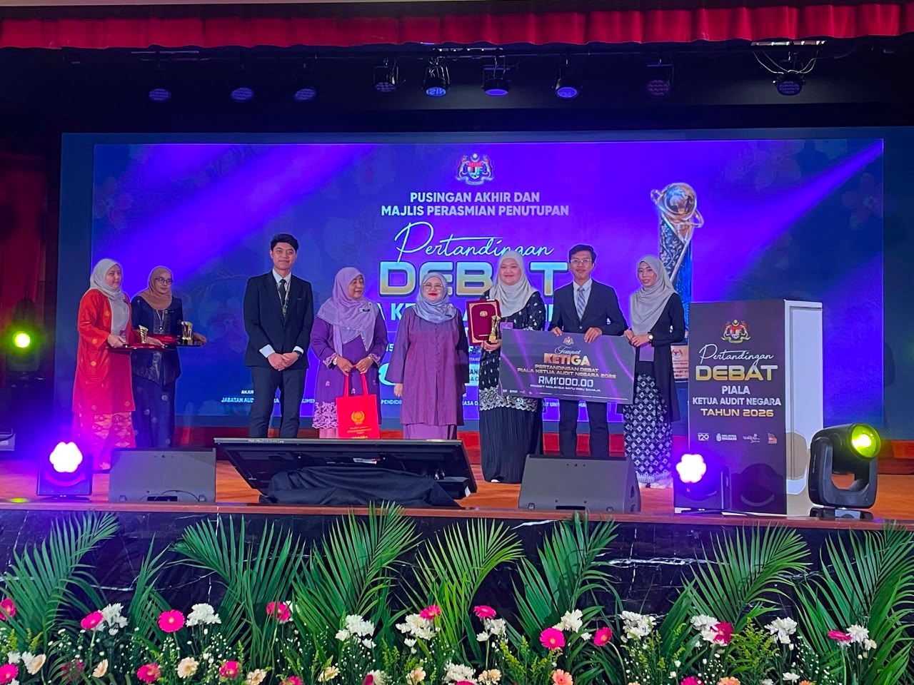 UiTM's debate team standing on stage while receiving their RM1,000 cash prize from the VIPs